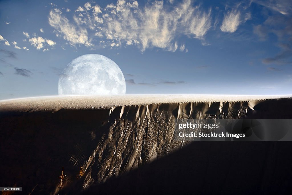 A larger than life depiction of the full moon rising above a sand dune at White Sands National Monument, New Mexico.