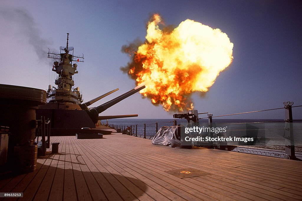A projectile is fired off the port side from one of the Mark 7 16-inch/50-caliber guns in the No. 1 turret aboard the battleship USS Wisconsin (BB-64) during a gunnery exercise. The ship is deployed in the gulf to support Operation Desert Shield.