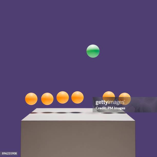 one green ball bouncing higher than 6 orange balls - wettbewerb konzepte stock-fotos und bilder