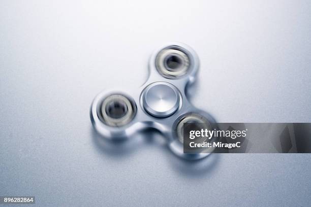 spinning silver colored fidget spinner - spinning top stock pictures, royalty-free photos & images