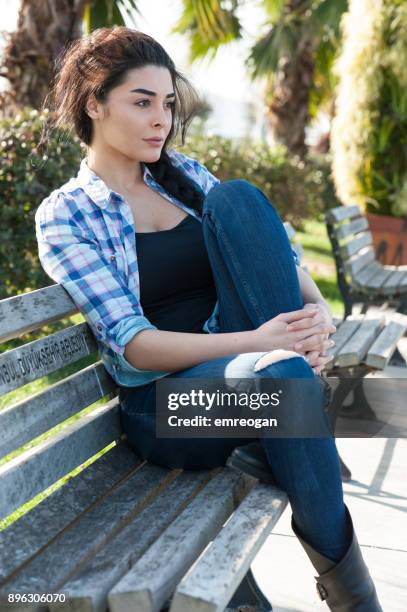 young woman sitting on a park bench - emreogan stock pictures, royalty-free photos & images