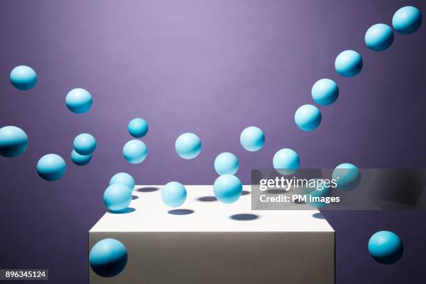 blue balls bouncing off of white cube - bouncing ball stockfoto's en -beelden