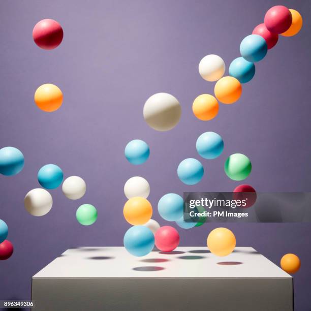 balls of various color bouncing off of white box - group of objects stock-fotos und bilder