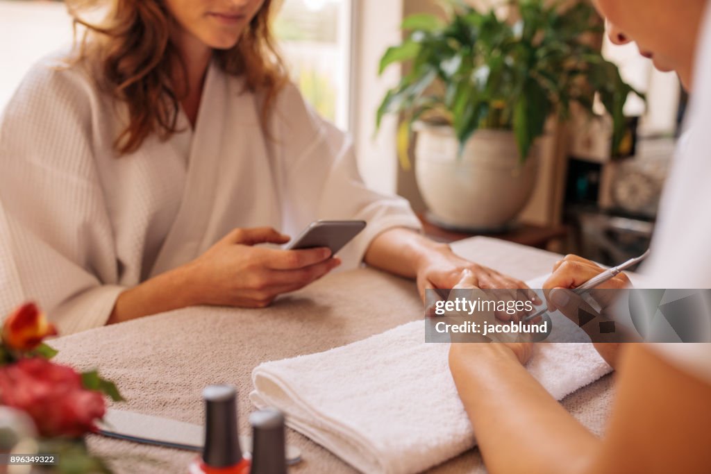 Woman using mobile phone during manicure at spa