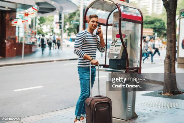 man is using public phone to call taxi or ride sharing service to get to hotel - australia taxi stock pictures, royalty-free photos & images