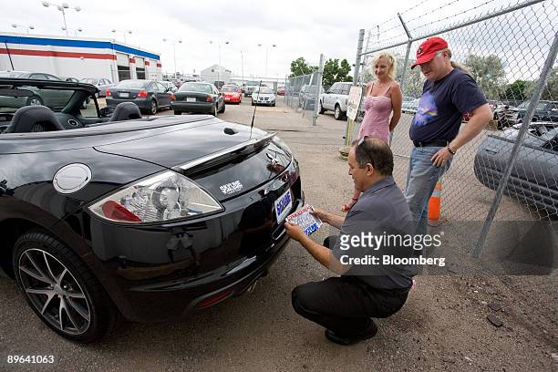 Salesman Ken Roybal places a temporary license on a Mitsubishi Eclipse purchased by Dori and Michael Houx, right, at Skyline Mitsubishi in Thornton,...