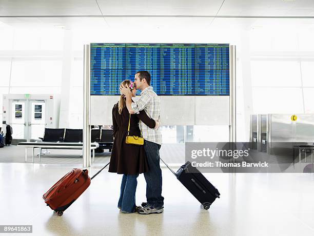 man kissing woman in airport near departure board - airport departure board stock pictures, royalty-free photos & images