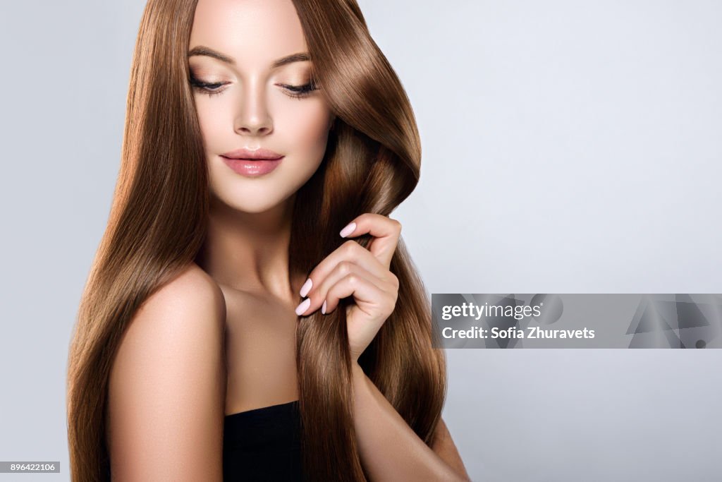 Young, brown haired beautiful model with long,  straight, well groomed hair is touching own hair with tenderness.