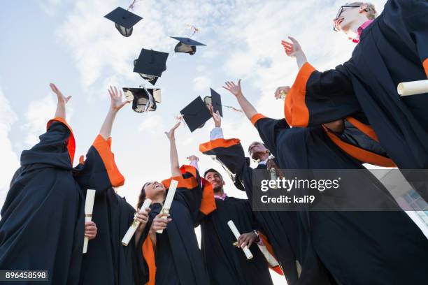 laureati adolescenti multietnici gettano berretti in aria - cappello nero foto e immagini stock
