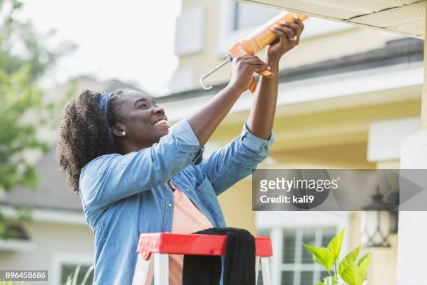 woman on ladder outside house doing repairs - caulk stock pictures, royalty-free photos & images