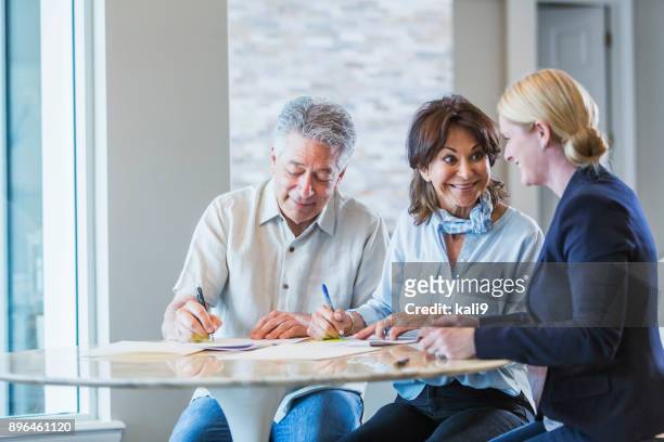 senior couple talking with a personal advisor, signing papers - man signing paper stock pictures, royalty-free photos & images