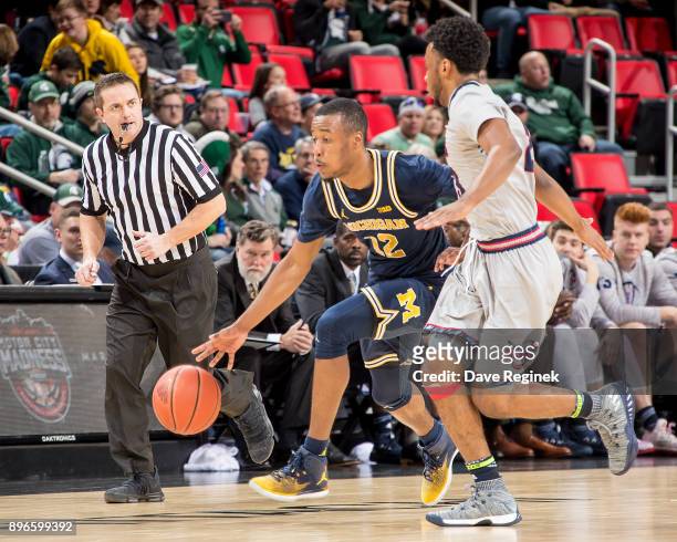 Muhammad-Ali Abdur-Rahkman of the Michigan Wolverines moves the ball up court next to Josh McFolley of the Detroit Titans during game one of the...