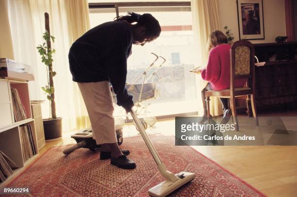 The inmigrant women´s works Inmigrant woman works of assistant in a house. She is cleaning a room with a hoover