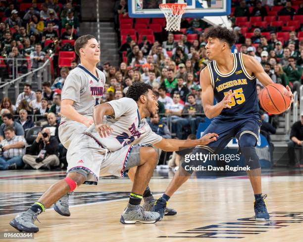 Eli Brooks of the Michigan Wolverines dribbles the ball up court next to Josh McFolley and DeShawndre Black of the Detroit Titans during game one of...