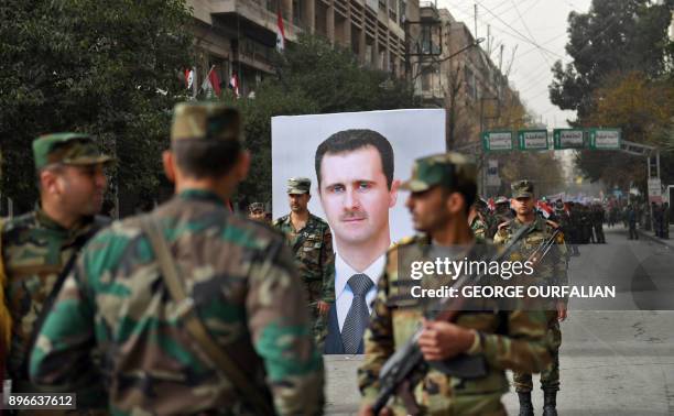 Syrian soldiers walk past a portrait of President Bashar al-Assad during a government celebration marking the first anniversary of the retaking of...