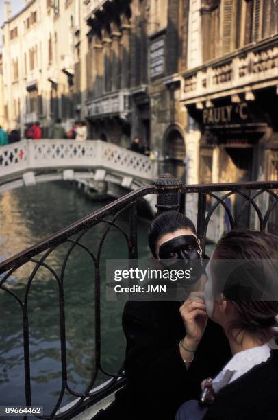 Carnivals in Venice A woman paints the face to another one in a channel of Venice during the carnivals