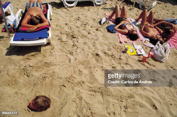 Poniente Beach. Benidorm. Alicante Beach scene: Tourists taking the sun and a boy playing buried in the sand