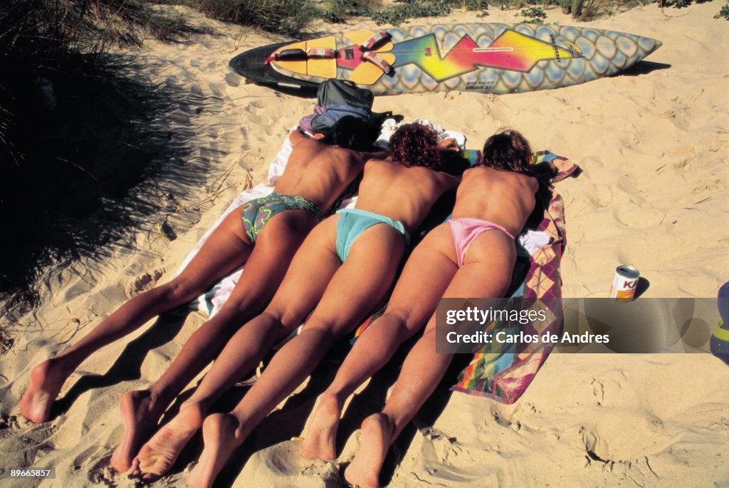 Girls sunbathing in a beach Three girls sunbath lay down on the sand of a beach