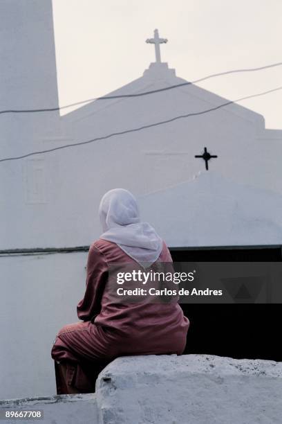 Muslim woman seated in front of a church View of a Muslim woman turned sitting in front of the facade of a Catholic church of Melilla