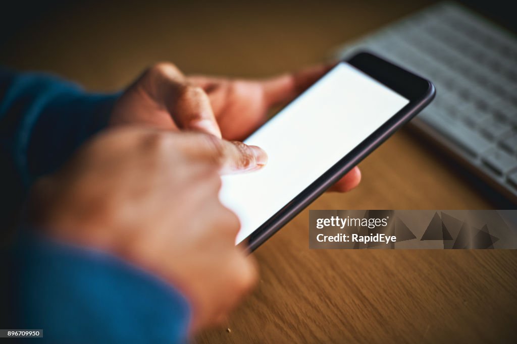 Male hands tap mobile phone screen, keyboard in background