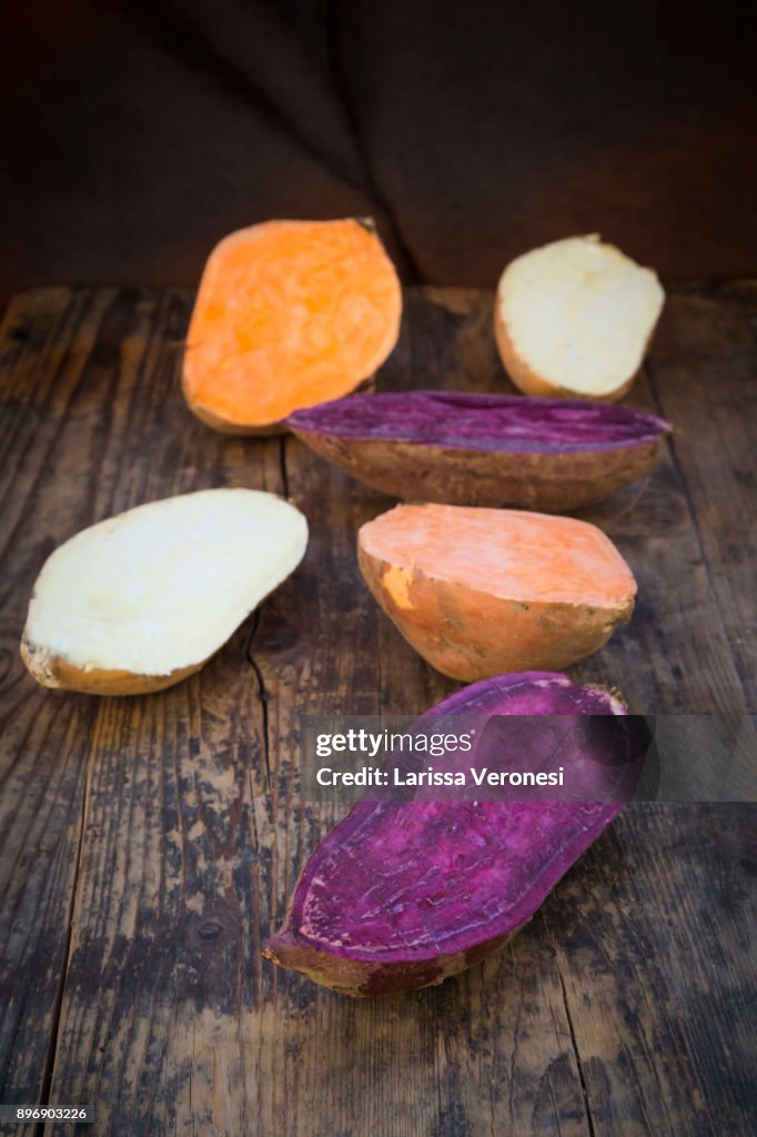 Different sweet potatoes on dark wood, cut in half