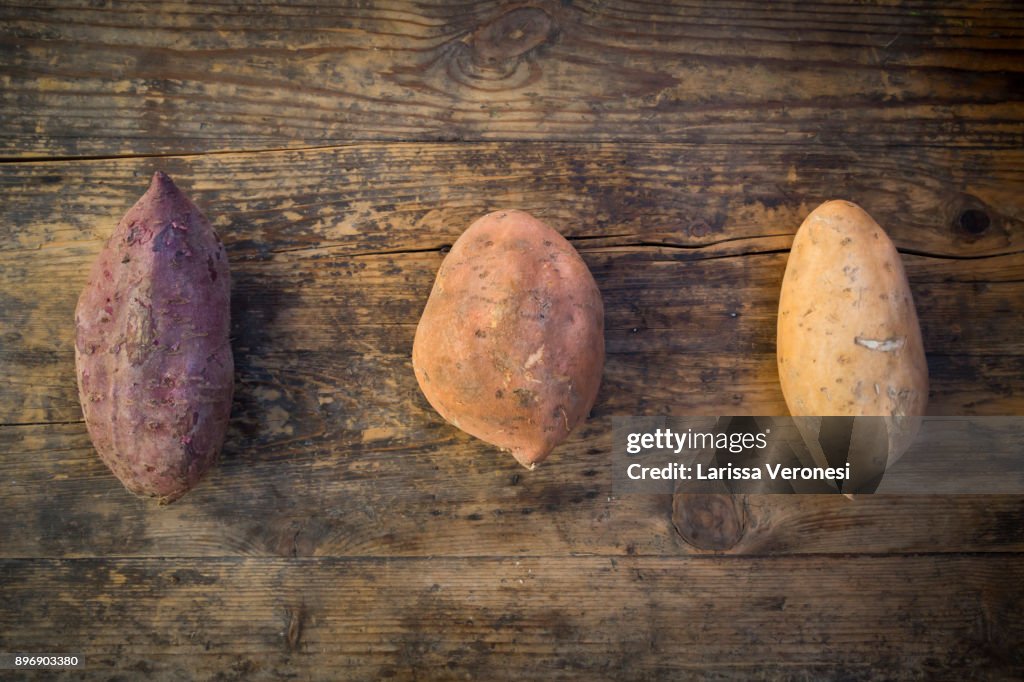 Different sweet potatoes on dark wood