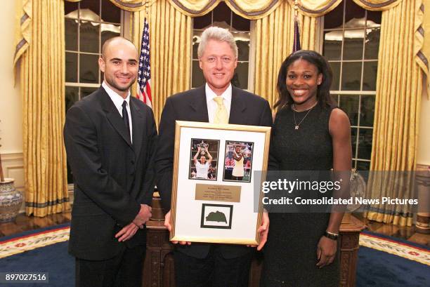 American politician US President Bill Clinton poses with US Open Tennis Champions Andre Agassi and Serena Williams in the White House's Oval Office,...