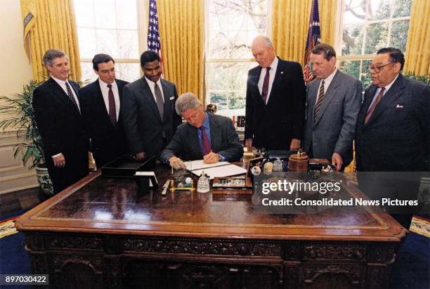 American politician US President Bill Clinton signs an executive order in the White House's Oval Office, Washington DC, April 16, 1997. Behind him...