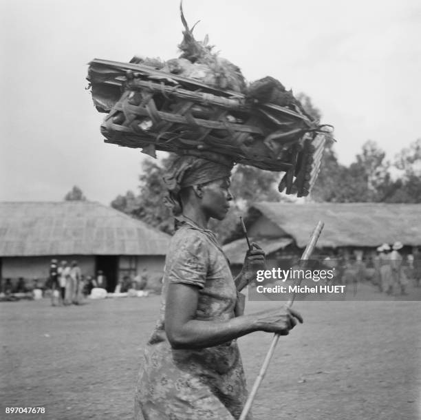 Femme portant une cage a poules sur la tete en Republique du Congo, circa 1950.