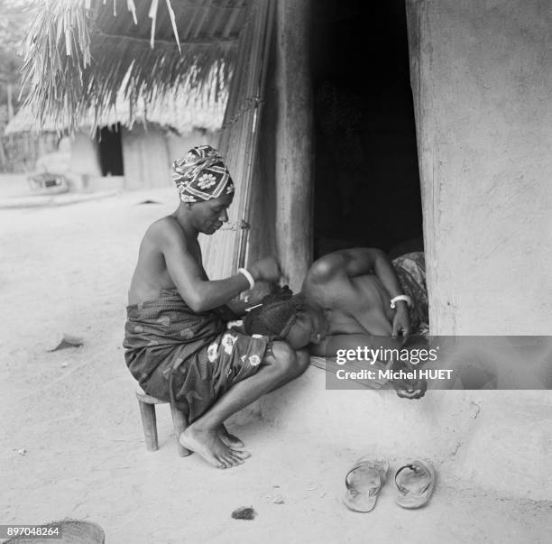Jeune femme se faisant coiffer en Cote d'Ivoire, circa 1950.
