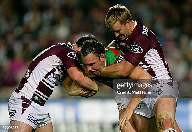 Ben Lowe of the Rabbitohs is wrapped up by the defence during the round 22 NRL match between the Manly Warringah Sea Eagles and the South Sydney...