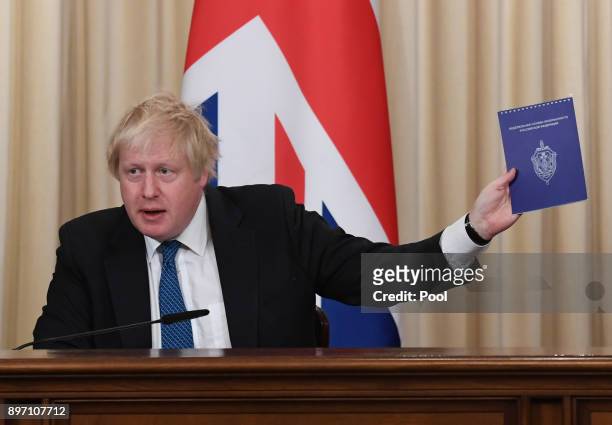 British Foreign Secretary Boris Johnsonholds up a publication featuring the emblem of Russia's FSB security agency during a press conference with his...