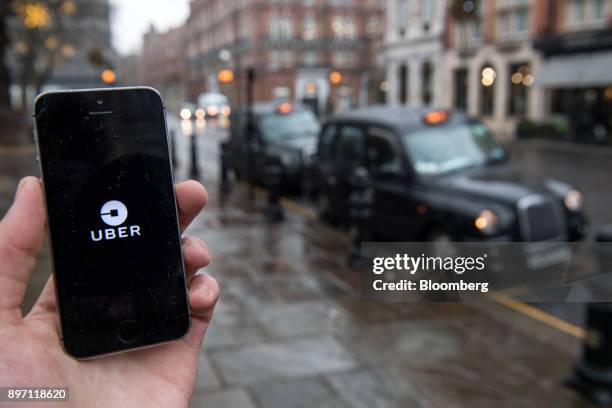 An Uber Technologies Inc. Logo sits on a smartphone display in this arranged photograph as London taxis sit parked beyond in London, U.K., on Friday,...