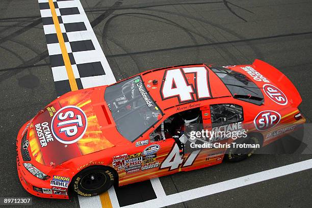 Marcos Ambrose, driver of the STP Toyota, grabs the checkered flag from the flagstand after winning the NASCAR Nationwide Series Zippo 200 at Watkins...