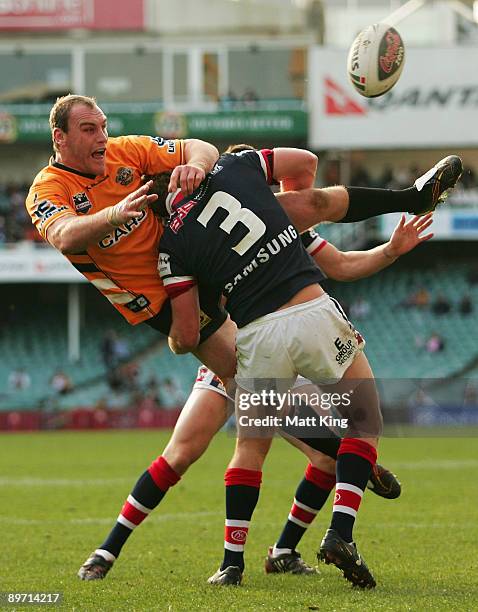 Gareth Ellis of the Tigers passes the ball as he is tackled heavily by Mitchell Aubusson of the Roosters during the round 22 NRL match between the...