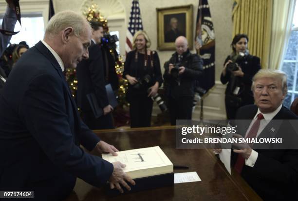 White House Chief of Staff John Kelly picks up documents off of United States President Donald J. Trump's desk during an event to sign the Tax Cut...