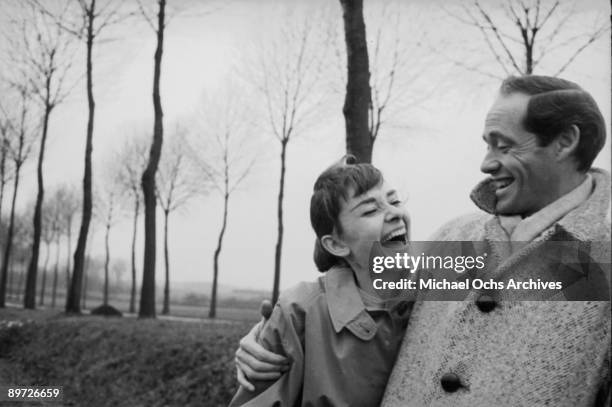 American actor Mel Ferrer buttons up his coat around his wife, actress Audrey Hepburn , on a country road outside Paris, 1956.