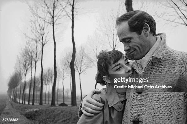 American actor Mel Ferrer buttons up his coat around his wife, actress Audrey Hepburn , on a country road outside Paris, 1956.