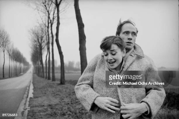 American actor Mel Ferrer buttons up his coat around his wife, actress Audrey Hepburn , on a country road outside Paris, 1956.