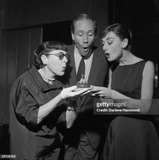 Hollywood costume designer Edith Head , American actor Mel Ferrer and his wife, Actress Audrey Hepburn , blowing out the candle on Head's birthday...