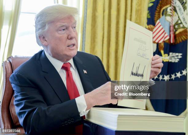 President Donald Trump holds up a tax-overhaul bill after singing it into law in the Oval Office of the White House in Washington, D.C., U.S., on...