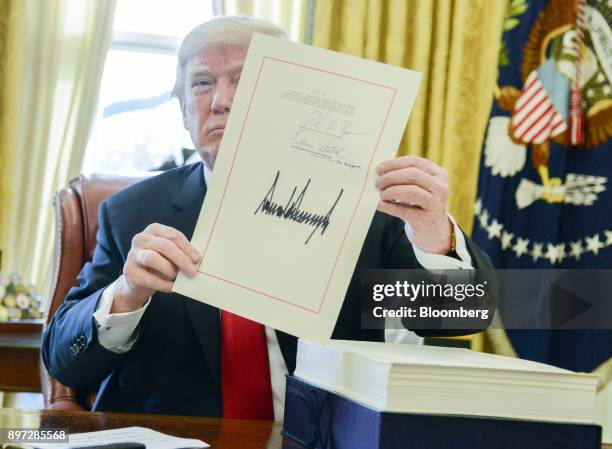 President Donald Trump holds up a tax-overhaul bill after singing it into law in the Oval Office of the White House in Washington, D.C., U.S., on...