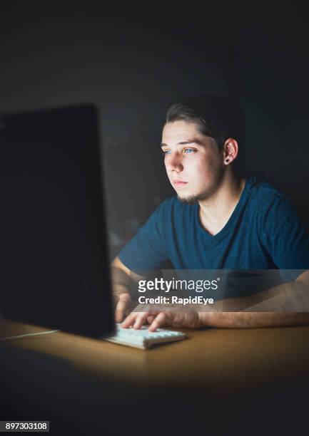 solitary young man working on computer by night - romance fraud stock pictures, royalty-free photos & images