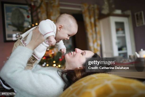 a 6 months old baby in the arms of his mum at home, in a christmas atmosphere - raising baby stock-fotos und bilder