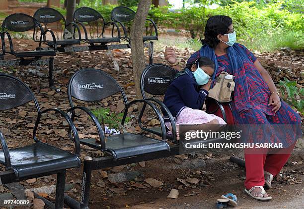 An Indian girl wearing a mask takes rest on her mother's lap as they queue at an H1N1 swine flu virus test centre at a government hospital in...