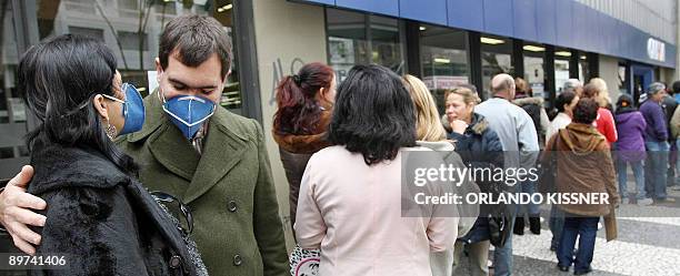 Customers wear surgical masks to combat the influenza A , as they queue outside a bank following a decision of the Labour Ministry to limit to 10 the...