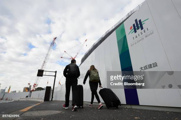 Pedestrians carrying luggage walk past the Taisei Corp. Logos displayed on a fence at a construction site in Tokyo, Japan, on Friday, Dec. 22, 2017....