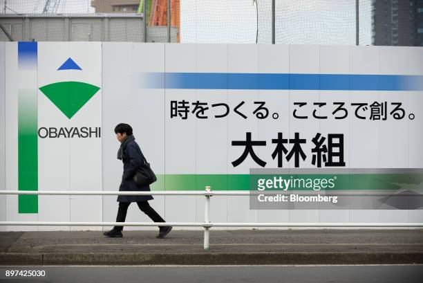 Pedestrian walks past the Obayashi Corp. Logo displayed on a fence at a construction site in Tokyo, Japan, on Friday, Dec. 22, 2017. A logo of...