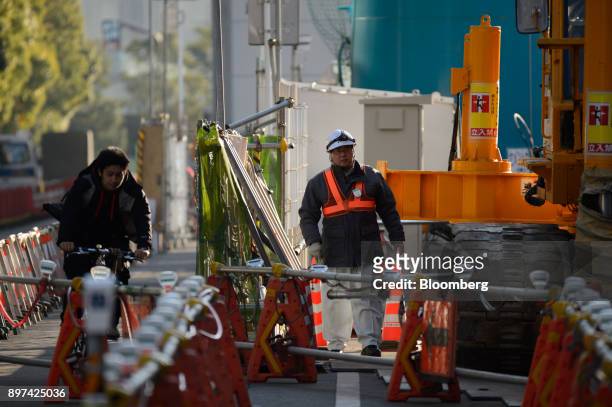 Cyclist rides past a worker walking at the construction site for magnetic levitation train tracks and platforms at Shinagawa Station in Tokyo, Japan,...
