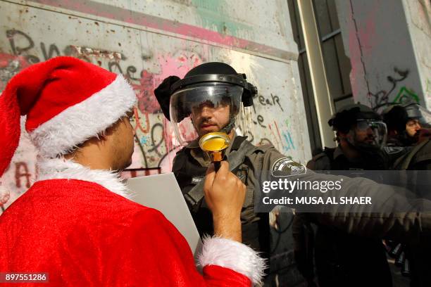 Palestinian protester dressed in a Santa Clause outfit confronts an Israeli borderguard during a demonstration at the main entrance of the West Bank...